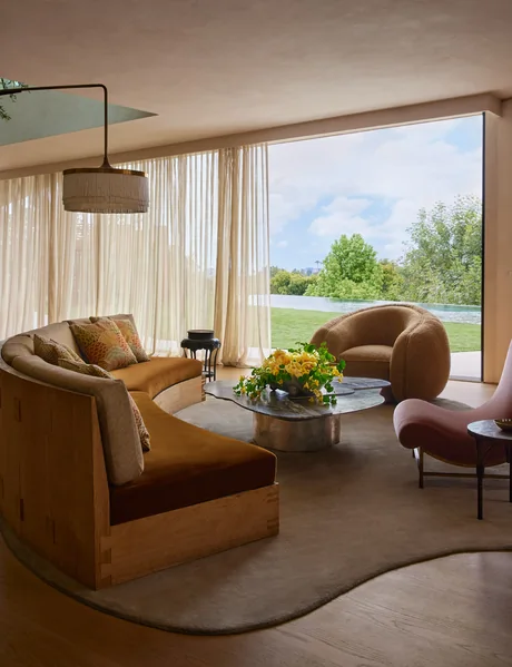 Curved neutral rug beneath a sofa and lounge chairs in a window-lined living room